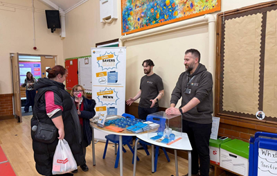 Cambrian Credit Union representatives discussing the School Savers scheme with a parent and pupil at a primary school.